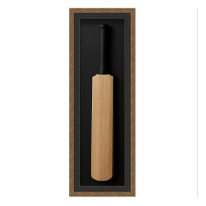 May include: A framed cricket bat. The bat is made of light-colored wood with a black grip. It is set against a black background within a brown wooden frame. The frame is rectangular and vertically oriented.