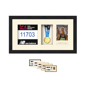 Könnte beinhalten: Eine schwarz gerahmte Präsentation mit einer Marathon-Startnummer mit der Nummer 11703, einer Goldmedaille mit blauem Band und einem Foto einer Läuferin. Der Rahmen enthält das New Balance-Logo und das TCS-Branding.