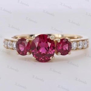 Könnte beinhalten: Ein goldener Ring mit einem großen, oval geschliffenen, leuchtend rosa Mittelstein, flankiert von zwei kleineren, rund geschliffenen rosa Steinen. Die Ringschiene ist mit einer Reihe kleiner, klarer, rund geschliffener weißer Steine besetzt.