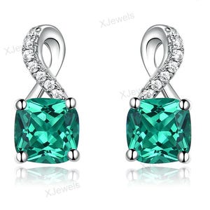 Puede incluir: Un par de pendientes plateados con una piedra preciosa verde de corte cojín montada en cuatro garras. La parte superior de cada pendiente tiene un diseño de infinito retorcido con pequeñas piedras blancas redondas.