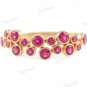 Peut inclure: Une bague en or ornée d'un groupe de multiples rubis roses ronds et vibrants, sertis individuellement dans des chatons. Les pierres sont disposées selon un motif organique et décalé sur l'anneau, créant un aspect texturé avec des montures en or poli.