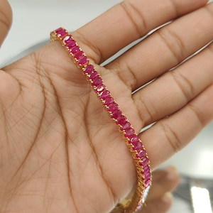 Op de afbeelding: Een gouden armband met een rij ovaal geslepen robijn edelstenen. De gouden zetting contrasteert met het dieprode van de robijnen, waardoor een luxueus sieraad ontstaat. Een klassiek ontwerp voor speciale gelegenheden.