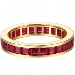 Puede incluir: Una alianza de oro amarillo con un engaste de canal continuo de rubíes rojos vibrantes de talla cuadrada. El anillo presenta un acabado metálico pulido con una hilera uniforme de piedras preciosas que rodea toda la circunferencia del aro.
