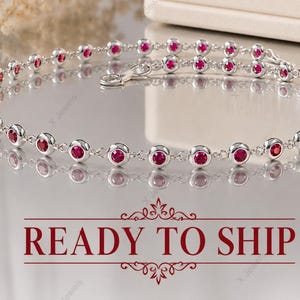 Peut inclure: Un bracelet en argent délicat orné de deux rangées de pierres rouges. Le bracelet présente des rubis ronds sertis, reliés par une fine chaîne en argent. Le texte "READY TO SHIP" est affiché en rouge. Mesure environ 15-20 cm.