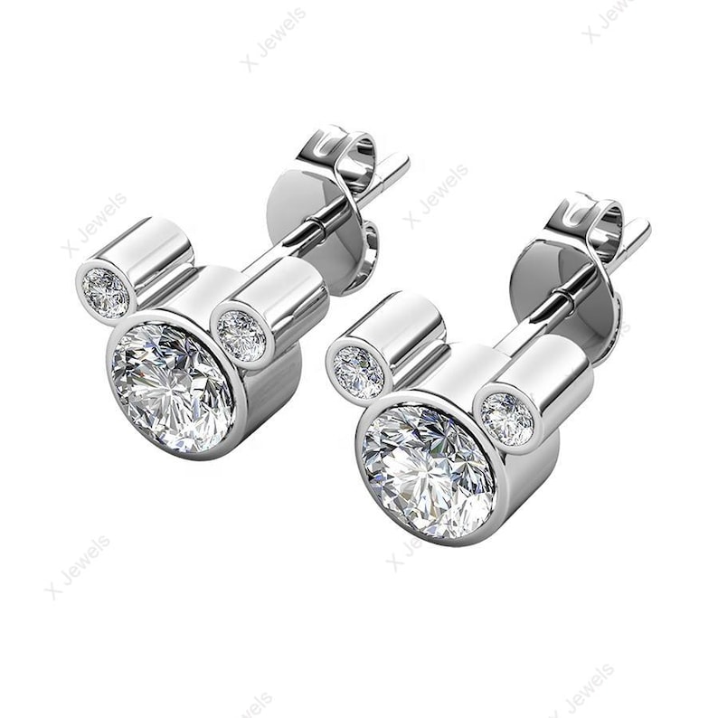 May include: A pair of silver-toned stud earrings. Each earring features a large, round, clear gemstone at the center, with two smaller gemstones above, forming a Mickey Mouse head shape. The gemstones sparkle brightly.