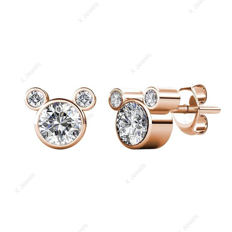 May include: A pair of silver-toned stud earrings. Each earring features a large, round, clear gemstone at the center, with two smaller gemstones above, forming a Mickey Mouse head shape. The gemstones sparkle brightly.