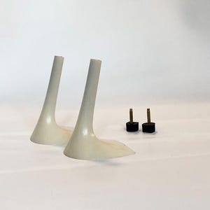 Pode incluir: Dois saltos de sapatos curvos em branco sujo, com base alargada e topo afilado. Também estão presentes duas pequenas pontas de salto pretas e castanhas. Os artigos estão sobre um fundo branco.