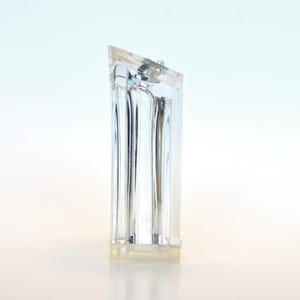 Op de afbeelding: Een heldere, rechthoekige kristallen flesstopper met een schuine bovenkant. De stopper is transparant, waardoor licht erdoorheen kan, en heeft een licht getextureerd uiterlijk. De basis is licht en doorschijnend.