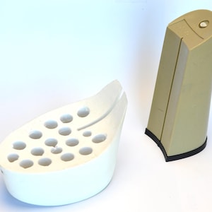 May include: A white shoe last with multiple holes and a tan shoe heel. The heel has a black rubber base. The objects are on a white surface.