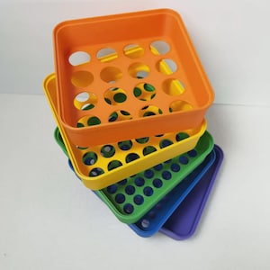 May include: A stack of colorful plastic trays in orange, yellow, green, blue, and purple. Each tray has a square shape with rounded corners and a series of circular holes. The trays are stacked at a slight angle, showcasing their vibrant colors.