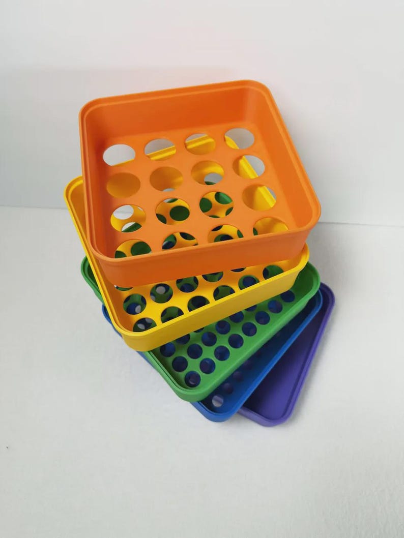 May include: A stack of colorful plastic trays in orange, yellow, green, blue, and purple. Each tray has a square shape with rounded corners and a series of circular holes. The trays are stacked at a slight angle, showcasing their vibrant colors.