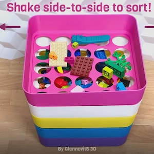 May include: A multi-colored plastic toy organizer with a pink top, white, yellow, blue, and purple base. The top has circular holes for sorting small toys. The text "Shake side-to-side to sort!" is above the organizer.