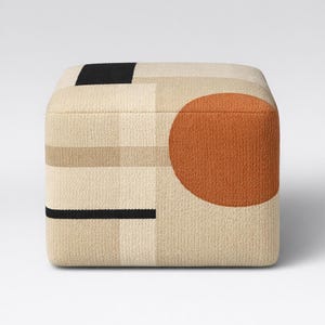 May include: A square ottoman with a geometric design. The ottoman features a beige background with a large orange circle on one side and black and tan geometric shapes. The ottoman is a cube shape and appears to be made of a textured fabric.