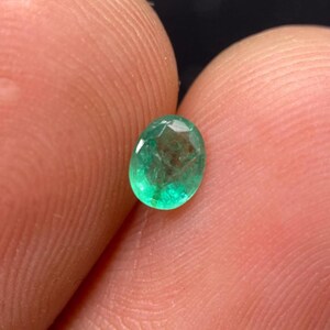 Könnte beinhalten: Ein kleiner, oval geschliffener Smaragd-Edelstein mit einer leuchtend grünen Farbe und sichtbaren inneren Einschlüssen. Der Edelstein verfügt über eine facettierte Oberfläche, die das Licht reflektiert und seine durchscheinende Qualität sowie den tiefgrünen Farbton unterstreicht.