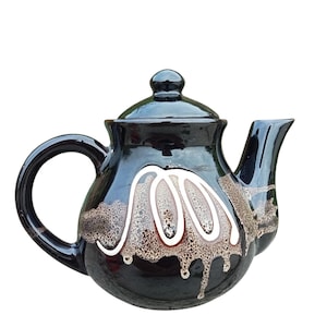 Pode incluir: Bule de cerâmica preto com acabamento brilhante. Apresenta um padrão decorativo branco e castanho no corpo, tampa a condizer e pega curva. O bico é curvo e o design é elegante. Ideal para servir chá.