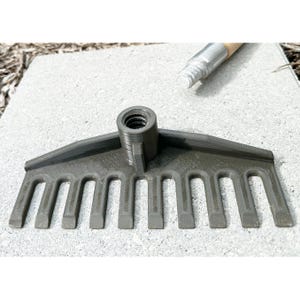 May include: A dark gray garden rake head with multiple tines, and a threaded socket for a handle. A silver and wood handle is partially visible in the background. The rake is designed for gardening and landscaping.