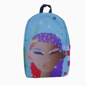 May include: A light blue backpack featuring a stylized illustration of a person's face with colorful hair and makeup. The backpack has a black handle, a green side pocket, and a red and white checkered side pocket.