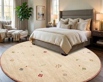 Puede incluir: Una alfombra redonda de color crema con un borde rojo y patrones geométricos dispersos en rojo, verde, azul y gris. La alfombra está en un dormitorio con una cama, una silla y una ventana.