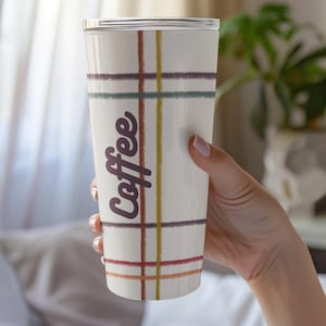 May include: A white travel mug with a plaid pattern in shades of red, yellow, green, and purple. The word "Coffee" is written vertically in a dark purple script. The mug has a silver lid.
