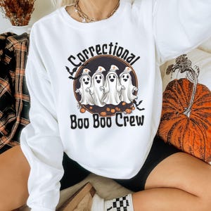 May include: White sweatshirt with a black and white graphic of ghosts wearing nurse hats and the text "Correctional Boo Boo Crew".