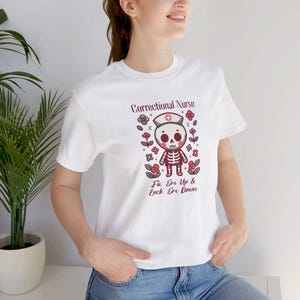 May include: White t-shirt with a cartoon skeleton wearing a nurse's hat and the text "Correctional Nurse Fix 'Em Up & Lock 'Em Down".