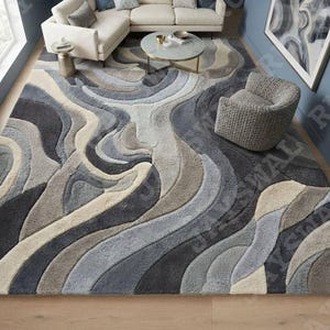 Könnte beinhalten: Ein großer Teppich mit texturiertem, mehrstufigem Flor und einem abstrakten, fließenden Wellenmuster in den Farben Anthrazit, Schieferblau, Beige und Creme. Der Teppich hat eine dicke, flauschige Oberfläche mit geschnitzten Konturen.