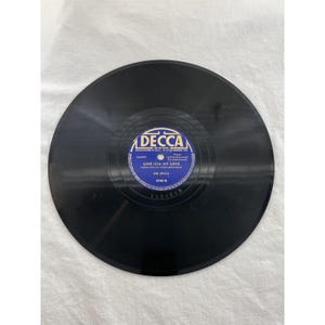 May include: A black vinyl record with a blue and white label. The label reads "DECCA" and "GIVE HER MY LOVE" by The Ink Spots. The record is a vintage music item, likely from the mid-20th century.