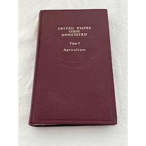 May include: A maroon-colored book titled "United States Code Annotated" with "Title 7 Agriculture" printed in gold lettering. The book has a textured cover and is slightly angled.