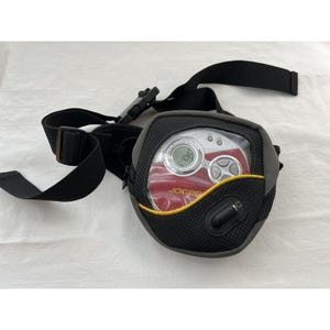 May include: A grey and black portable CD player with a clear window, red interior, and silver buttons. The player is in a black and grey bum bag with a black strap and buckle. The display reads "109".