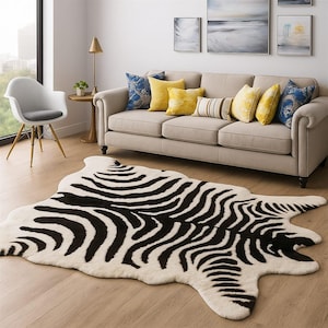 Peut inclure: Un tapis crème avec un motif zébré noir. Le tapis est dans un salon avec un canapé beige, des coussins décoratifs et une chaise blanche. Les dimensions du tapis sont d'environ 152 cm sur 203 cm.