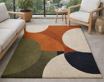 May include: A rectangular outdoor rug with a geometric design. The rug features large, overlapping shapes in shades of orange, green, cream, and navy blue. The rug is placed on a tiled patio, with outdoor furniture visible in the background.
