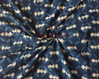 May include: Close-up of a navy blue fabric with a repeating pattern of white and light blue shapes. The fabric is gathered and twisted in the center, creating folds and shadows. The pattern appears to be hand-printed or block-printed.