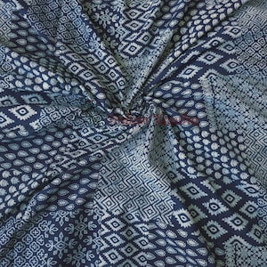May include: A close-up of a navy blue and white patterned fabric. The fabric is folded and features various geometric and floral designs. The patterns include diamonds, circles, and other shapes. The fabric is likely cotton or a similar material.