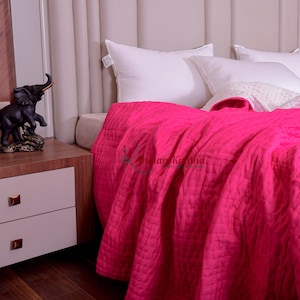 Könnte beinhalten: Ein Bett ist mit weißen Kissen und einer leuchtend pinkfarbenen, gesteppten Decke gemacht. Eine dunkle Elefantenstatue steht auf einem Nachttisch aus Holz mit weißen Schubladen. Das Bett steht vor einem gepolsterten, beigefarbenen Kopfteil.