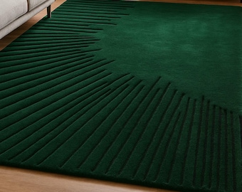May include: A large, emerald green area rug with a textured, linear design radiating from one side. The rug is placed on a hardwood floor in a living room setting, with a gray sofa and black cabinet visible.