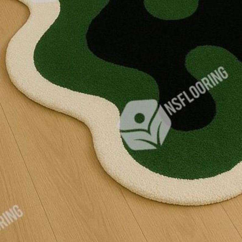 May include: A close-up of a modern rug with an abstract design. The rug features a cream-colored border, surrounding a pattern of green and black shapes. The text "NSFLOORING" is visible on the rug.