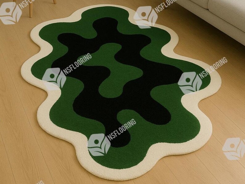 May include: A modern, abstract area rug with a unique, organic shape. The rug features a pattern of dark green, medium green, and black shapes, outlined with a cream-colored border. The rug is placed on a light-colored wooden floor.