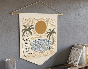Puede incluir: Un tapiz de pared color crema con temática de surf. El diseño presenta una tabla de surf, palmeras, un sol y olas del océano en tonos marrones y azules. El texto "SURF ALL DAY EVERY DAY" está impreso en la tabla de surf. El tapiz está suspendido de un palillo de madera.