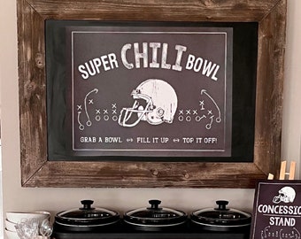 May include: A football-themed food station with three slow cookers on a copper stand. The cookers are on a green football field-themed table runner. A sign reads "Concession Stand Tackle Your Appetite". A chalkboard sign above the cookers reads "Super Chili Bowl Grab a Bowl Fill It Up Top It Off!"