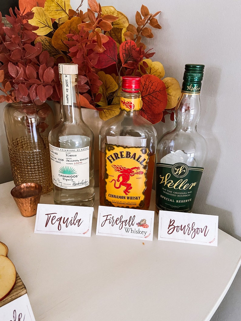 May include: Three bottles of liquor with labels: Tequila, Fireball Cinnamon Whiskey, and Weller Special Reserve Bourbon. The bottles are arranged on a white surface with small signs in front of them.