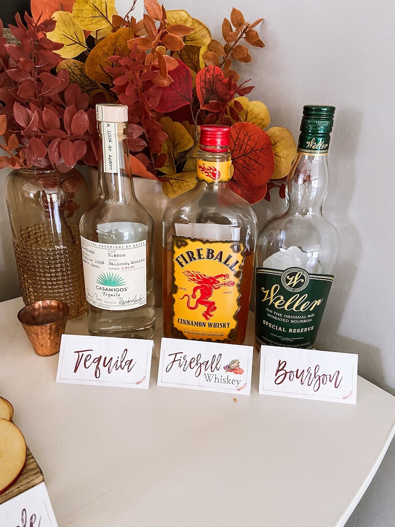 May include: Three bottles of liquor with labels: Tequila, Fireball Cinnamon Whiskey, and Weller Special Reserve Bourbon. The bottles are arranged on a white surface with small signs in front of them.
