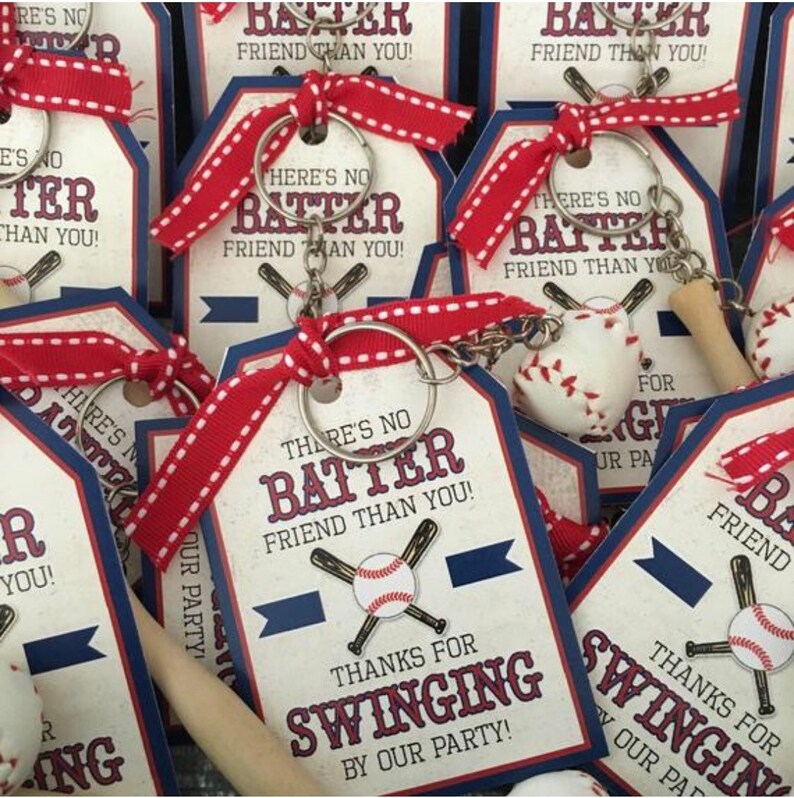 K&ouml;nnte beinhalten: Baseball-Schl&uuml;sselanh&auml;nger mit rotem und wei&szlig;em Band. Die Schl&uuml;sselanh&auml;nger-Anh&auml;nger sind blau und wei&szlig; mit dem Text "There's no batter friend than you!" und "Thanks for swinging by our party!"