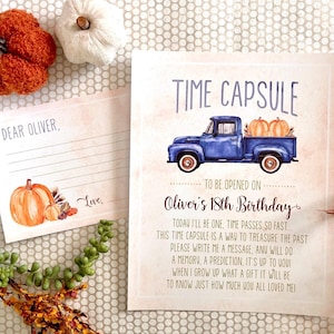 Op de afbeelding: Een afdrukbare tijdcapsulekaart met een blauwe pick-up truck die pompoenen vervoert. De kaart heeft de tekst "Time Capsule" en "Te openen op de 18e verjaardag van Oliver".