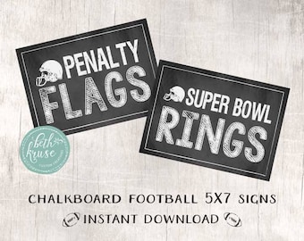 May include: Two black chalkboard signs with white text. The first sign says "Penalty Flags" with a football helmet graphic. The second sign says "Super Bowl Rings".