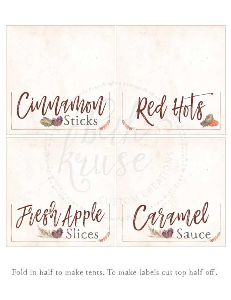 May include: Four printable tent cards with fall-themed designs. The cards feature the text "Cinnamon Sticks", "Red Hots", "Fresh Apple Slices", and "Caramel Sauce".