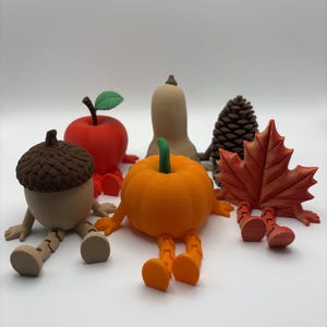 May include: A collection of six articulated figures shaped like autumn items: a brown acorn, a red apple with a green leaf, a tan butternut squash, a brown pinecone, an orange pumpkin with a green stem, and a red maple leaf, all with jointed legs.