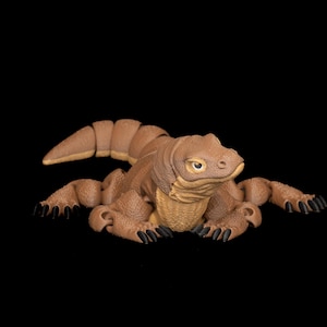 Peut inclure: Figurine de dragon de Komodo marron avec un corps texturé détaillé, des griffes et une longue queue. Le reptile a un ventre brun clair et des yeux jaunes. La figurine est posée sur un fond noir.