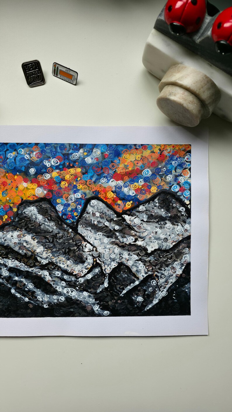 May include: An abstract painting of a mountain range with a colorful sky. The mountains are depicted in shades of gray and white, while the sky features swirls of orange, blue, and yellow. Two pins are visible.