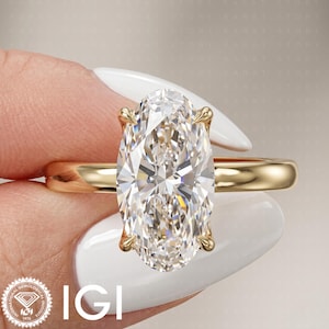 Op de afbeelding: Een gouden ring met een grote, ovaal geslepen, heldere edelsteen die door vier pootjes wordt vastgehouden. De ringband is van glad, gepolijst geelgoud. De afbeelding bevat het IGI-logo in de linkerbenedenhoek en de tekst KARAT STORY op de achtergrond.