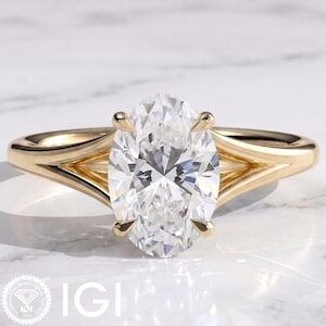 Op de afbeelding: Een geelgouden ring met een grote, kleurloze, ovaal geslepen middensteen die door vier klauwen wordt vastgehouden. De ringband heeft een gespleten ontwerp dat taps toeloopt naar de middensteen, wat zorgt voor een strakke, gepolijste afwerking.